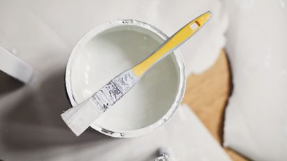 An open tin of white paint with a brush laid on top