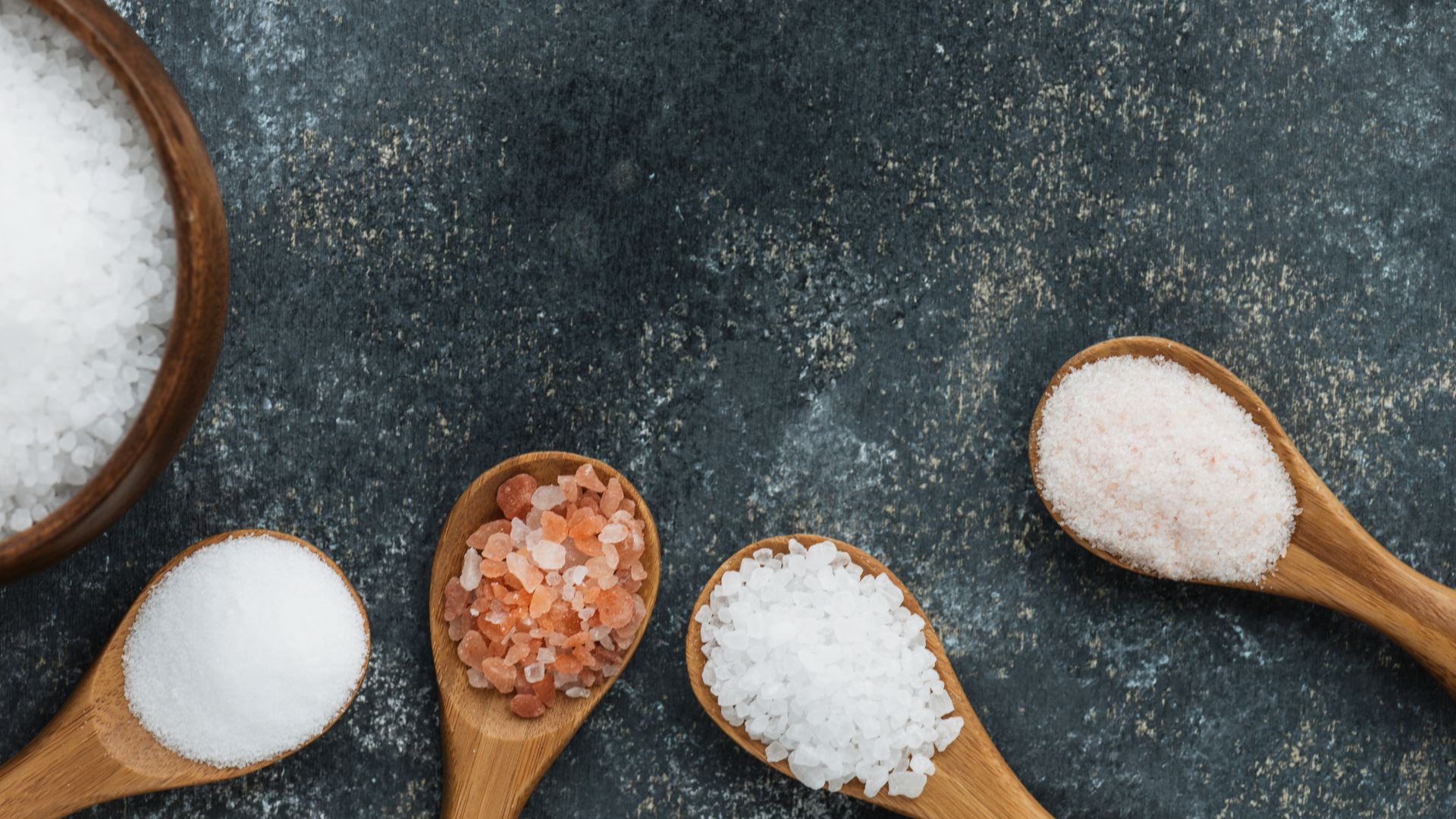 Flatlay image of different types of salts on wooden spoons