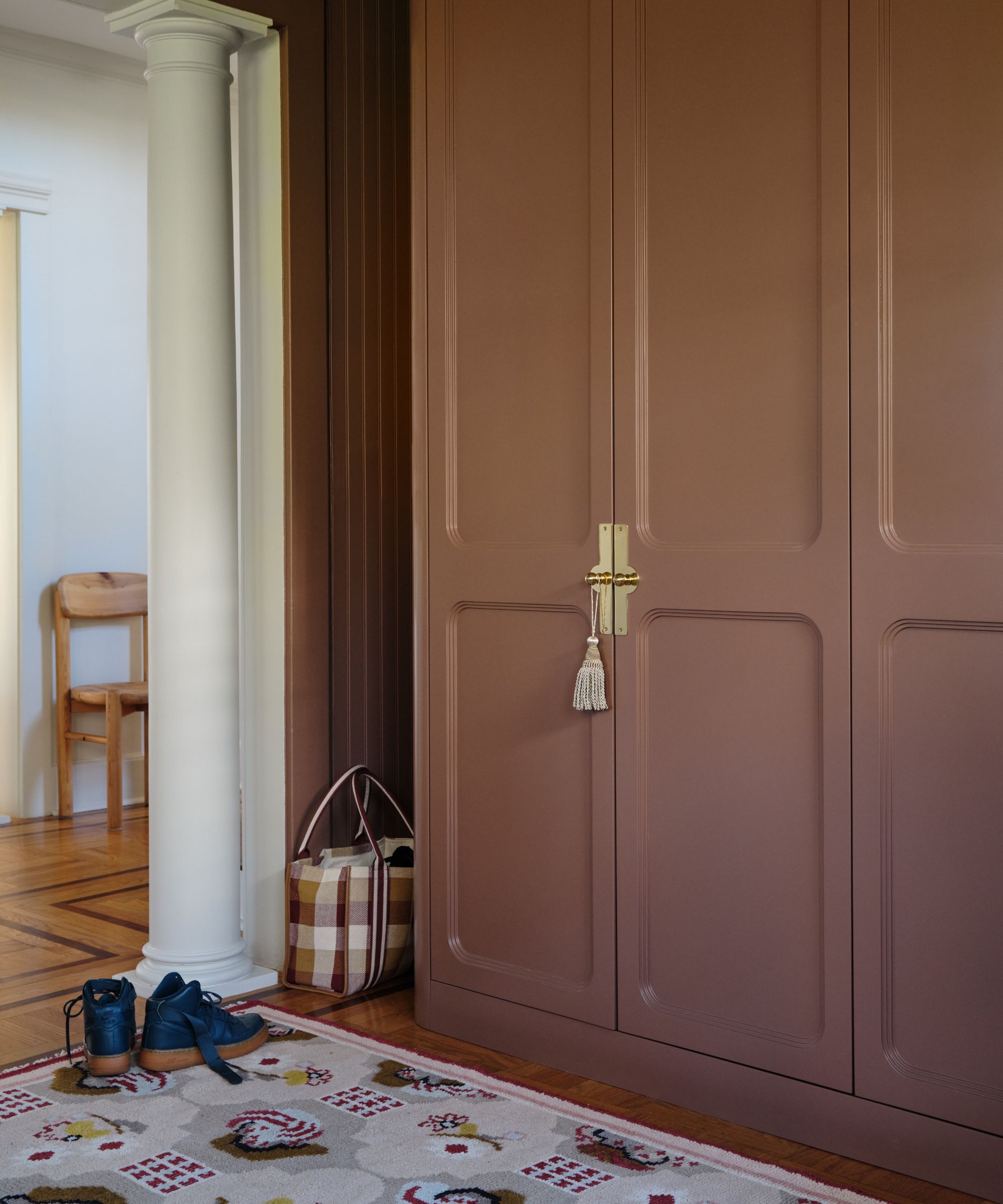 Mudroom with brown painted cupboards with gold handles, wooden floor, a folk-style rug, and a white pillar