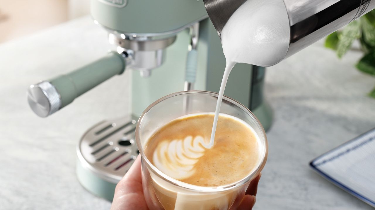 Person som h&auml;ller mj&ouml;lk i en latte gjord med De'Longhi Dedica Duo espressomaskin.