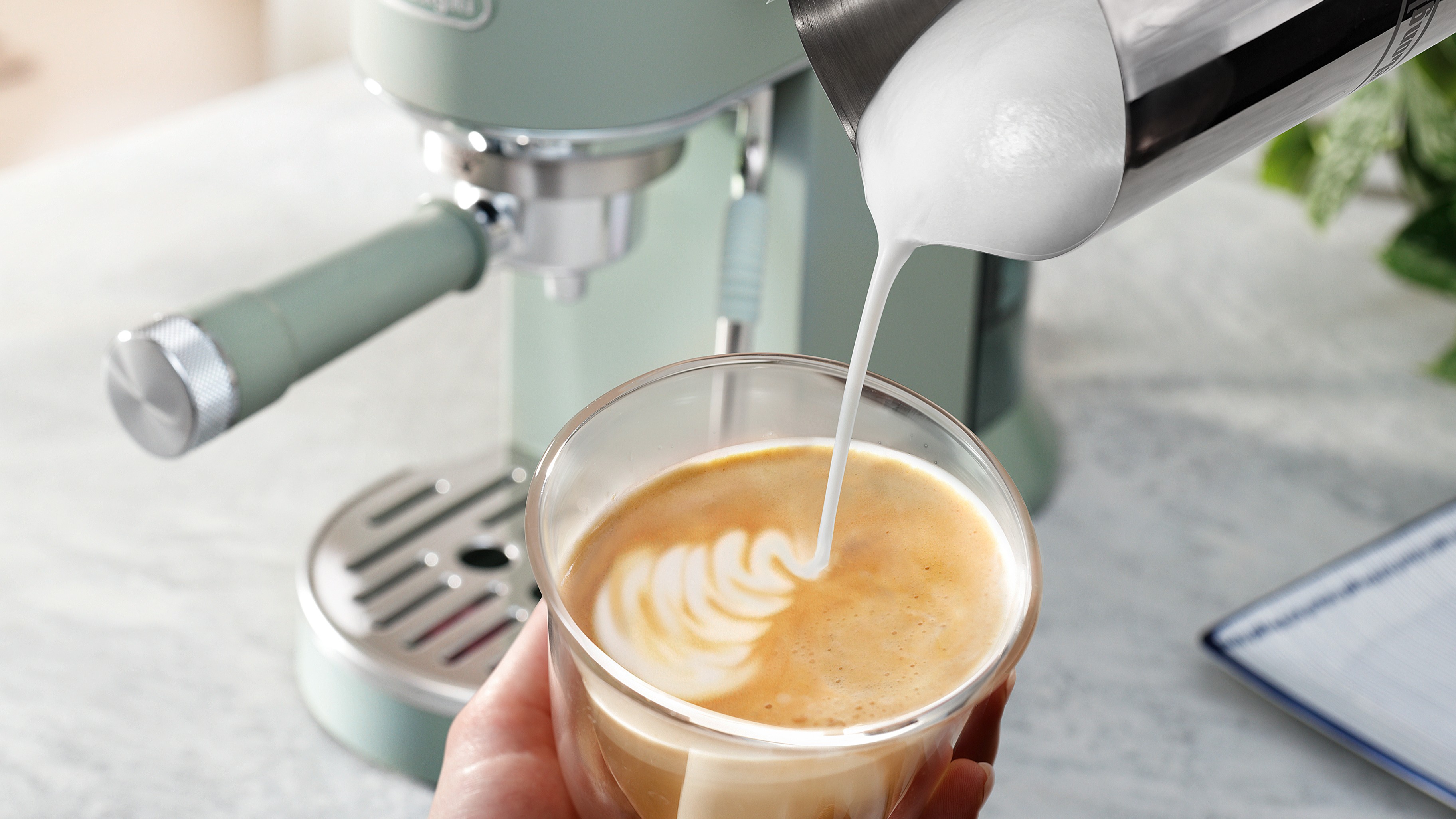 Person pouring milk into latte made using De'Longhi Dedica Duo espresso machine