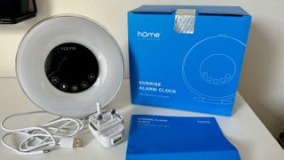 Unboxed HomeLabs alarm clock next to white plug and cable, blue instruction manual and blue box.