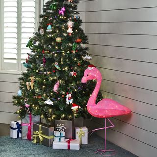 christmas tree on grey floor mat decorated with pink flamingo light and gift boxes