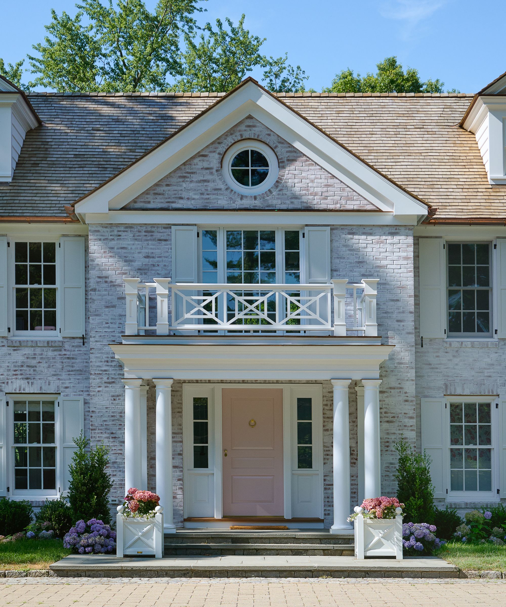 A home exterior with gray bricks, white trim, and a light pink front door.
