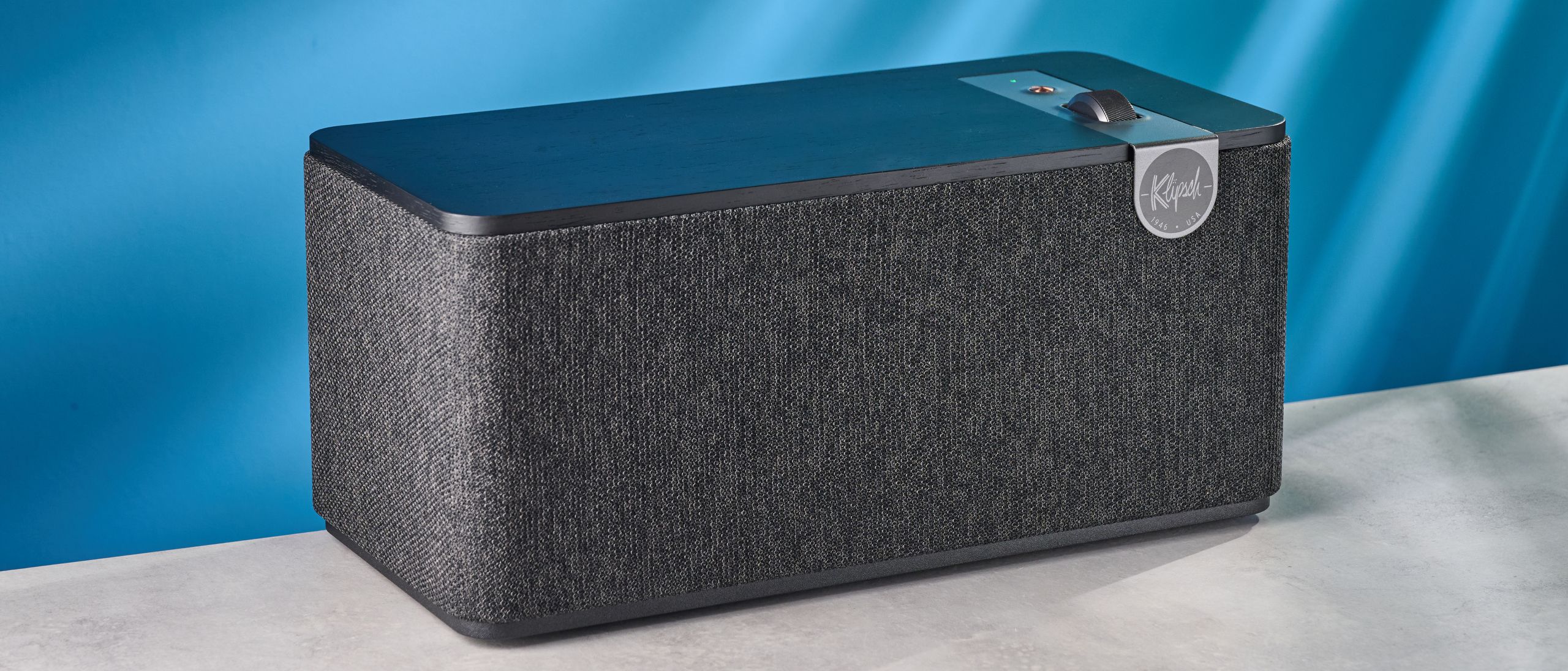 Klipsch The One Plus Bluetooth speaker in matte black photographed in front of a blue background.