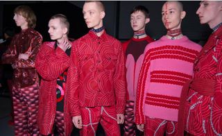 Group of male models stood together in a studio wearing pink & red clothing