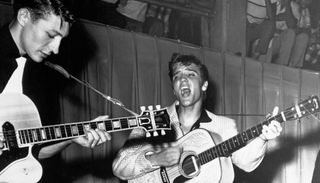 Scotty Moore (left) and Elvis Presley perform onstage at Fort Homer Hesterly Armory in Tampa, Florida on July 31, 1955