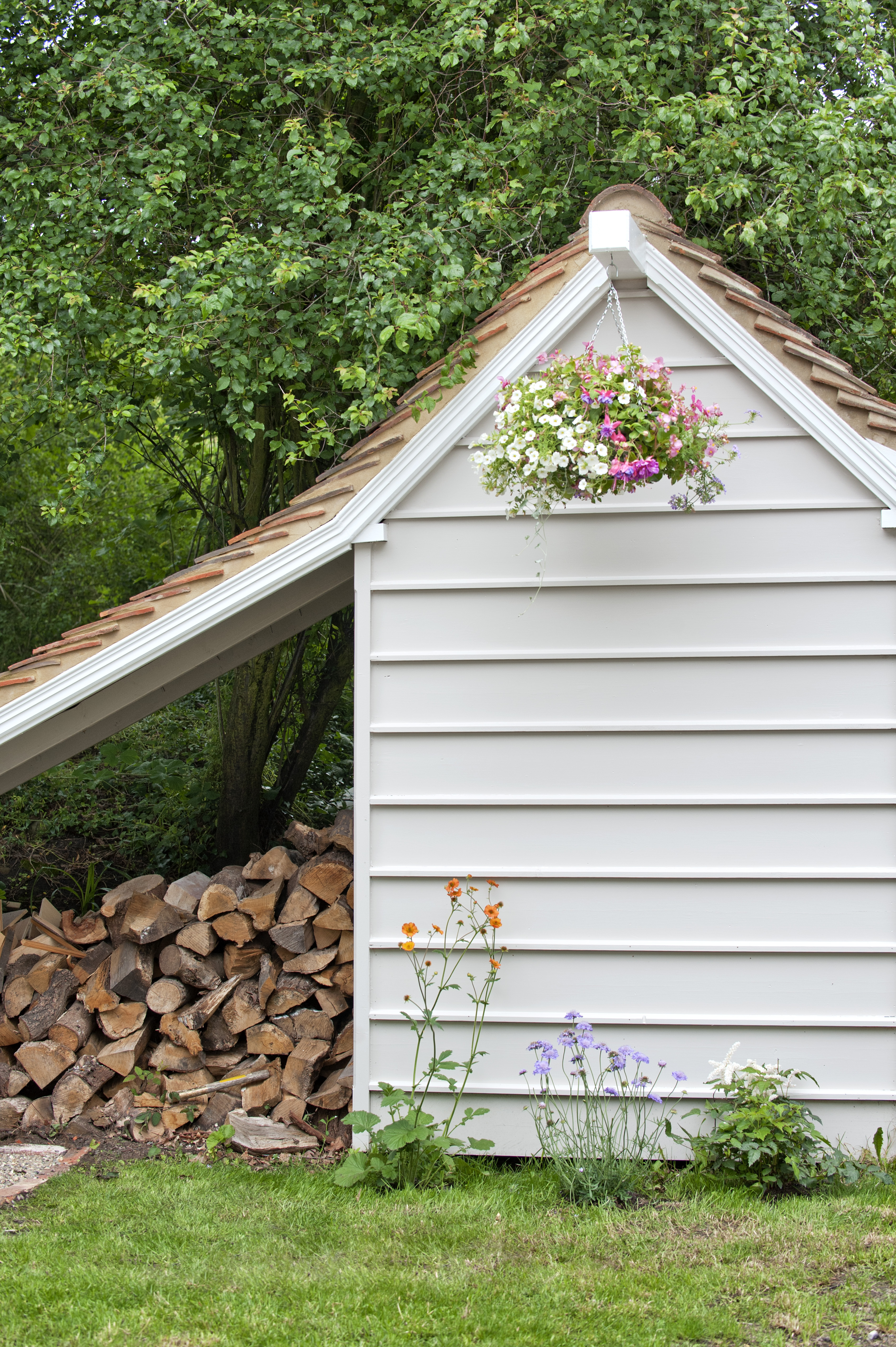 A cream paneled outbuilding next to a pile of logs