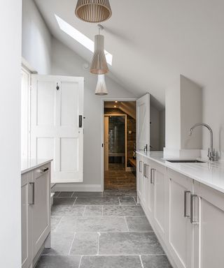 Kitchen units in white, a flagstone floor and storage units in a utility room.