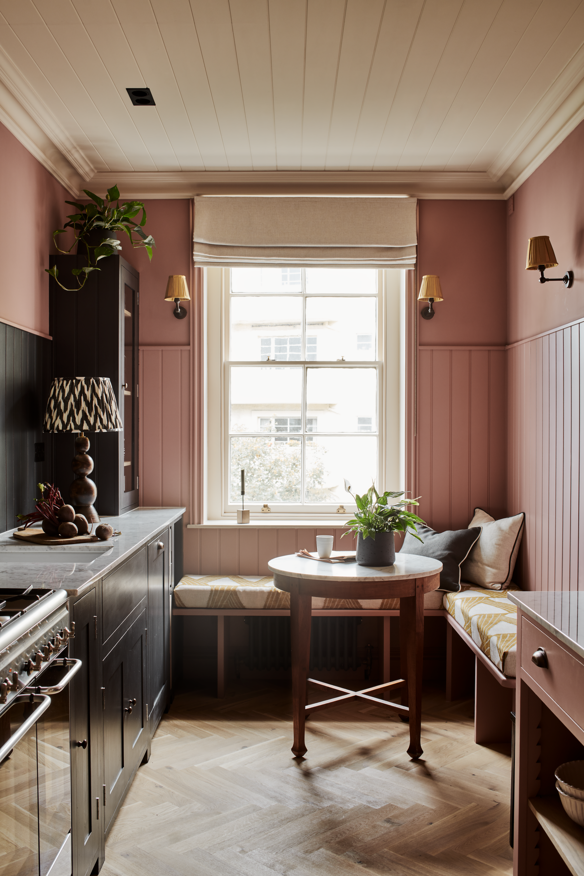 A small cosy pink and black kitchen with a sash window and window seat at the back