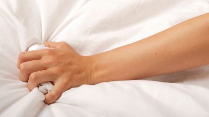 woman's hand gripping bedsheet