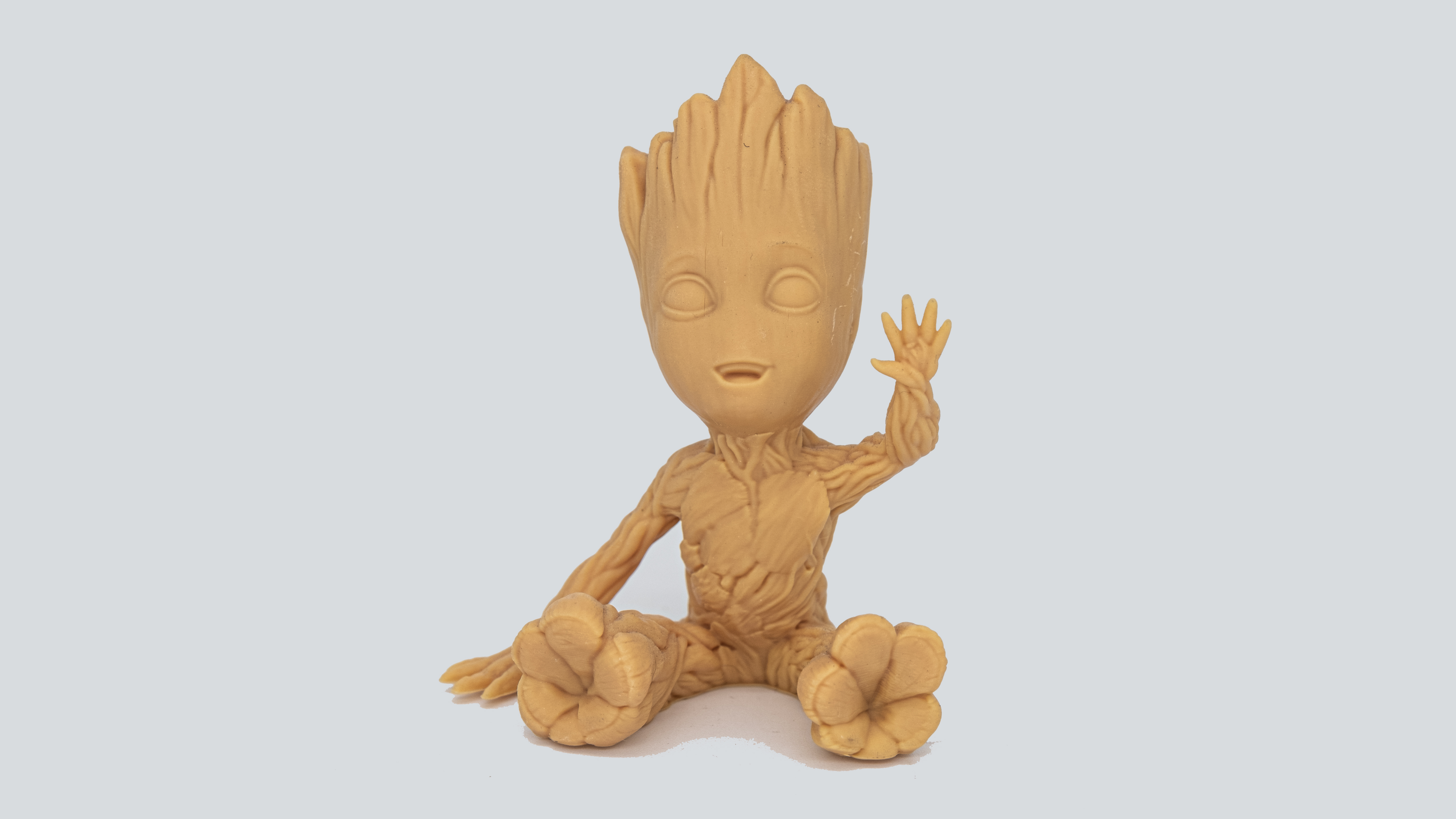 A sitting 3D-printed Baby Groot waving