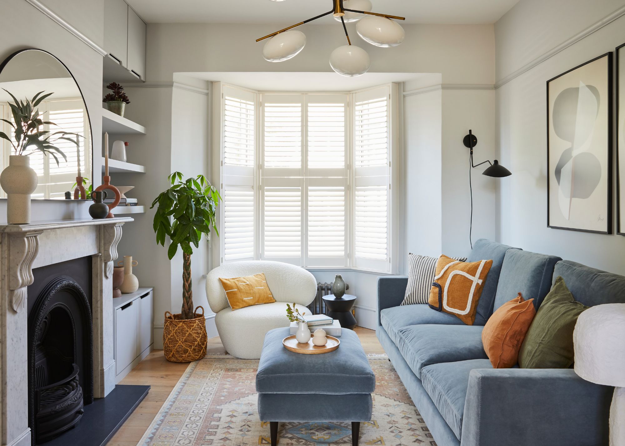 modern living room with white walls, bay window with white shutters, mid-blue sofa and ottoman