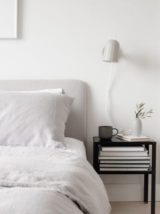 white bedroom with black bedside table, white linen, white wall light