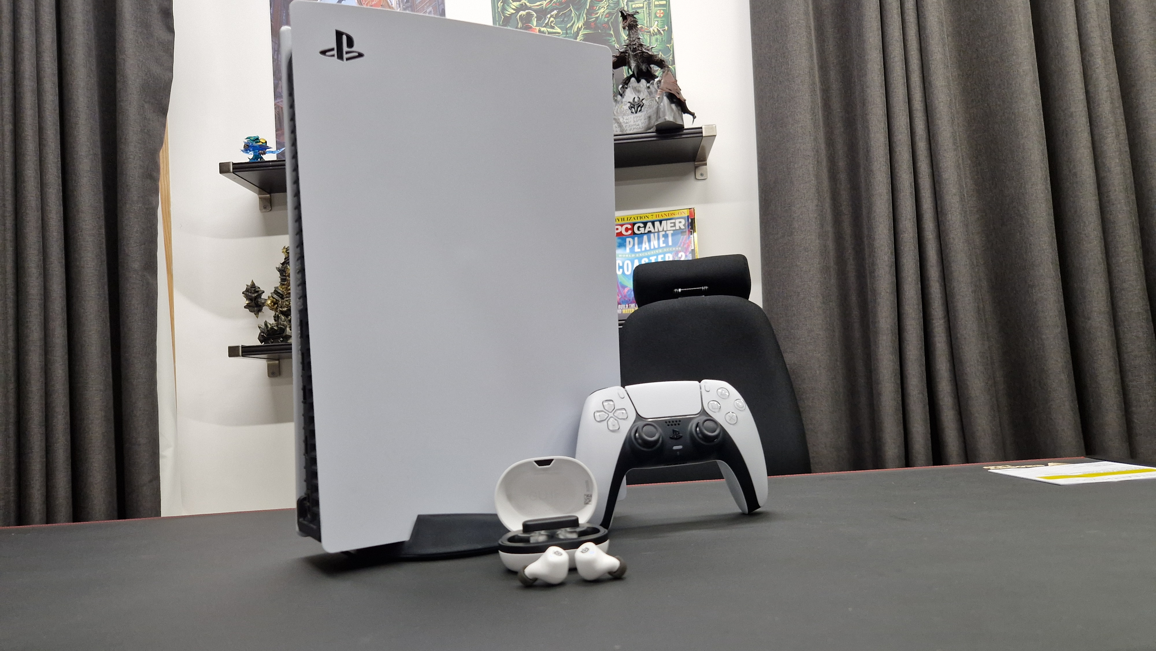 SteelSeries Arctis GameBuds on a black desk in front of a PS5 and DualSense