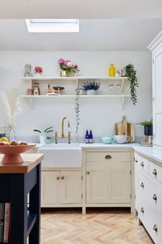 A white shaker kitchen with two white open shelves featuring plants, and various stylish kitchen accessories and utensils