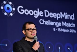 Demis Hassabis speaking at a conference with a microphone in hand