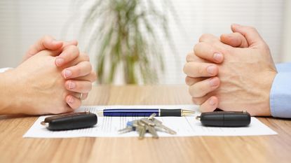 A man and a woman sit across one another with hands clasped on top of divorce papers.