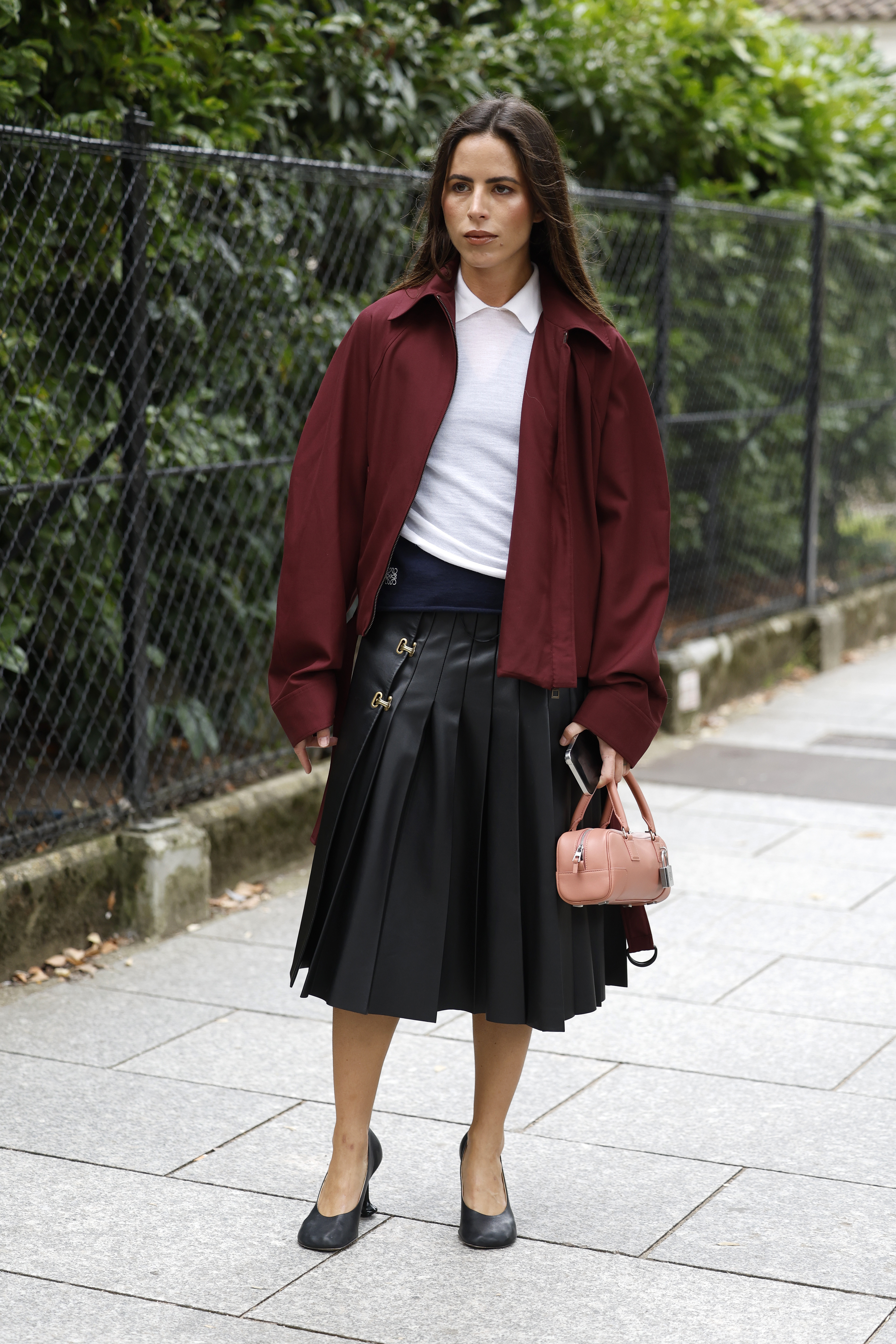 a woman wearing a white polo shirt, black pleated kilt, maroon jacket, and black heels