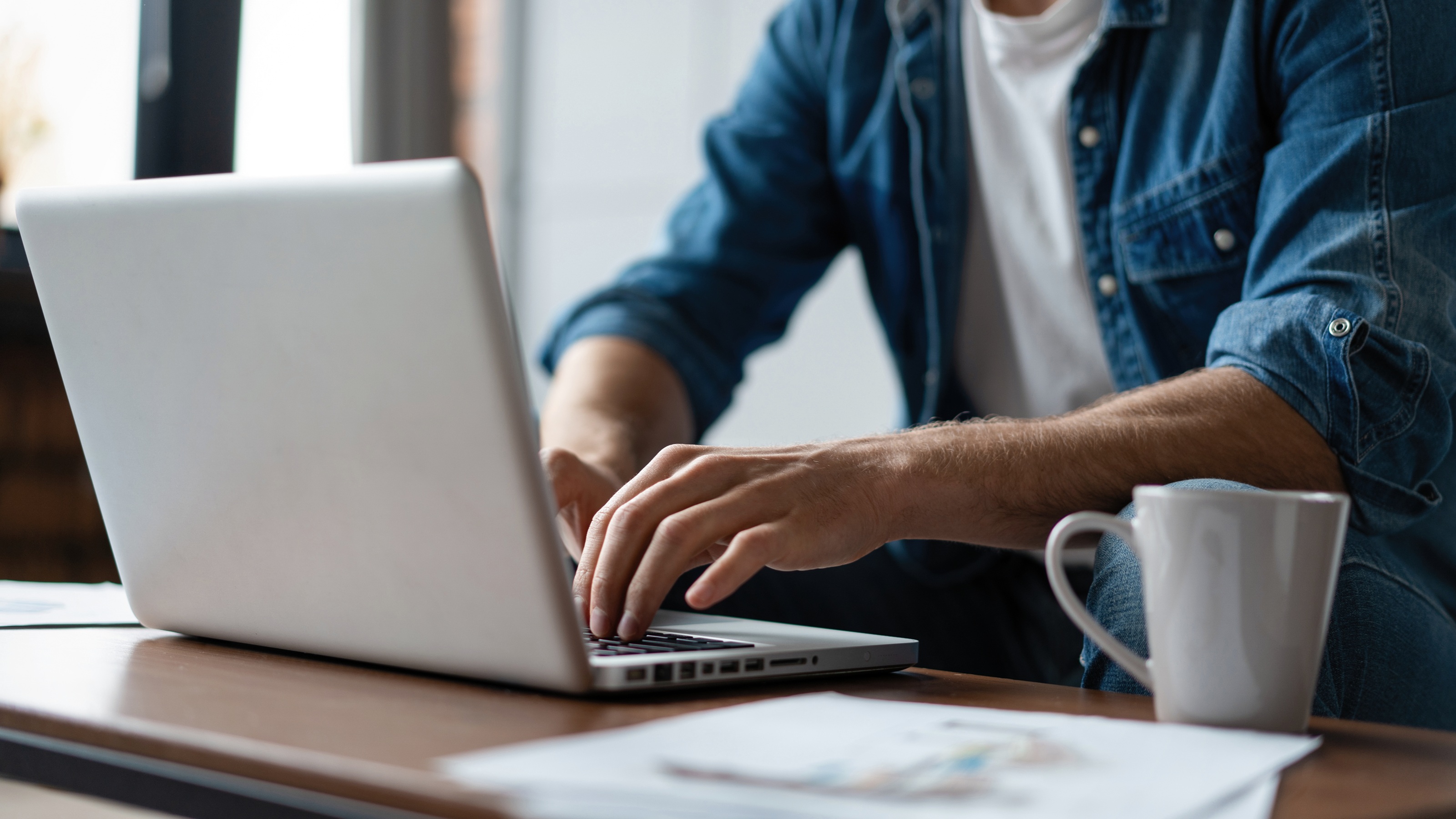 A man sits in front of his coffee table and works on a laptop.