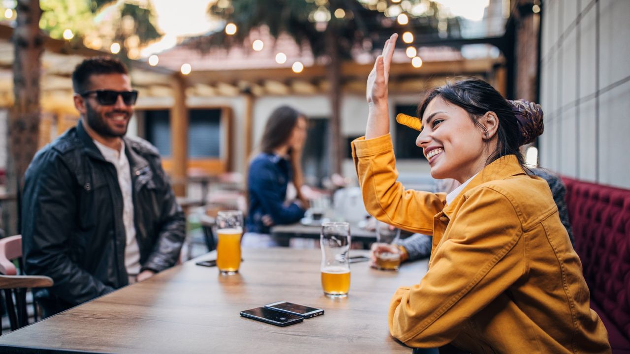 A man and a woman sitting outdoors at a bar, drinking beer together