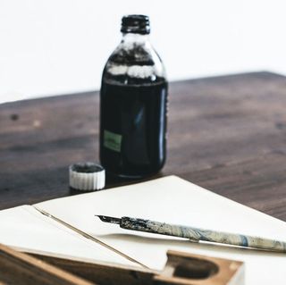 image of ink pen on paper with an ink bottle on a desk