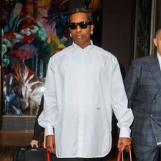 Asap Rocky steps outside wearing a red Chanel bag with a white shirt and black trousers.