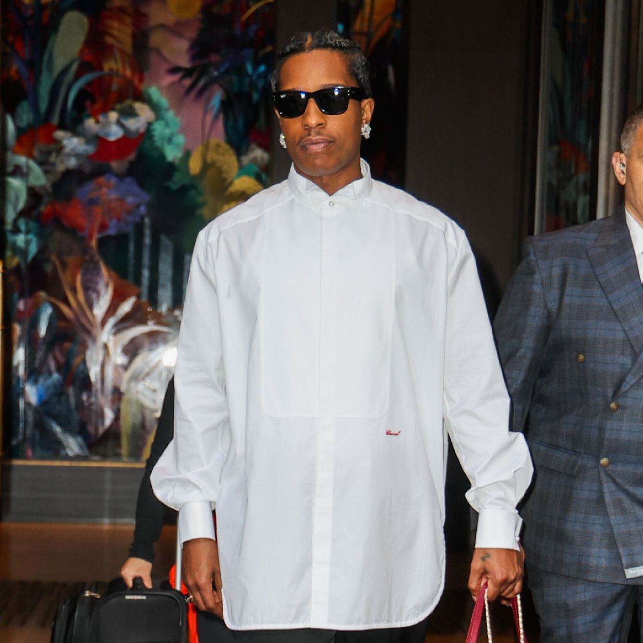 Asap Rocky steps outside wearing a red Chanel bag with a white shirt and black trousers.