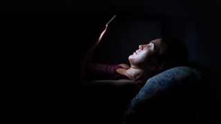 A woman lying in the dark, her face illuminated by the light from her phone screen.
