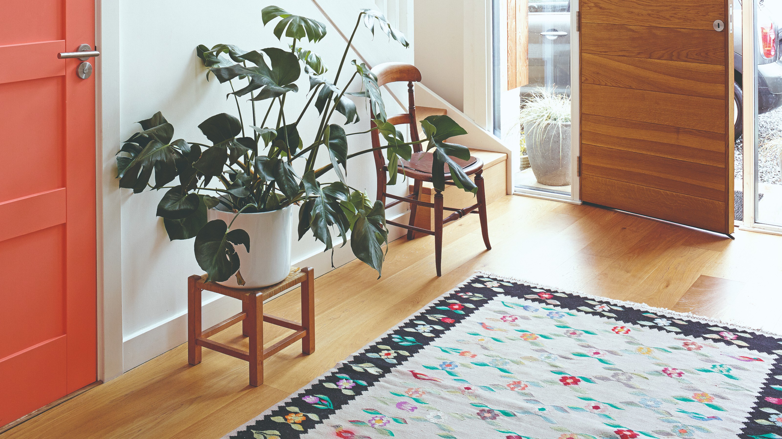 A spacious hallway with a large plant, a patterned runner and a coral door