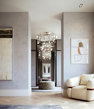 Living room with white armchair, grey walls, wall mirror and chandelier.