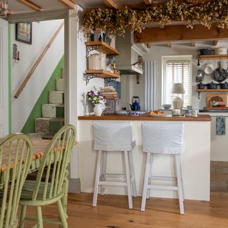 breakfast bar of a cottage kitchen with hops hanging from ceiling above beside original wooden staircase