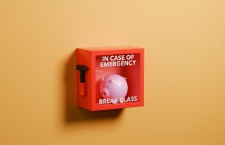 Conceptual image of a pink piggy bank inside of a red box with glass cover and a hammer with text saying "In Case Of Emergency Break Glass". Emergency funds concept