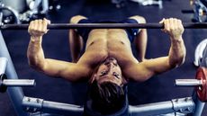 Shirtless men performing bench press in gym