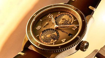 A close-up of Montblanc's new watch with rotating globes at the top and bottom of the watch face and a mini-timer circle on the left. Right side is a square for the date. The watch face is brown in colour with light brown arms. The face has 10, 2, 4, 8 numerals and a small line at 55, 5, 25, 35 and 45. The outer ring has a brown colour with light colour for the N, E, S, W locations. The watch-strap is dark-leather brown.