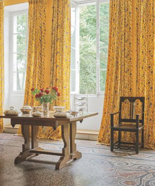 French dining room with yellow floral drapes, table laid out with silverware, tiled floor, open windows, yellow walls, antique chair