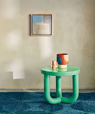 Textured cream walls, blue carpet, bright green modern side table, colorful pottery, square painting on wall