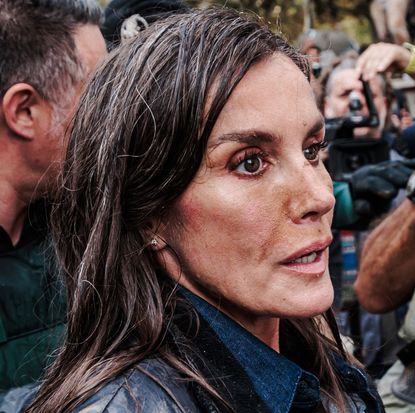 Queen Letizia wearing a mud-stained jacket and wet hair in a crowd of people