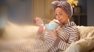 Woman with hair in towel relaxes at night with a bowl of cereal