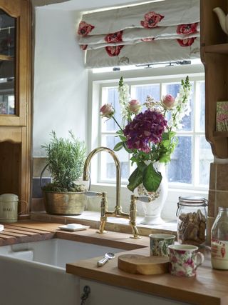 Butlers sink with gold taps, herbs and roses in window and vintage mugs