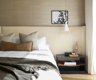 Neutral bedroom with black nightstand, modern lamp, and books on the below shelf
