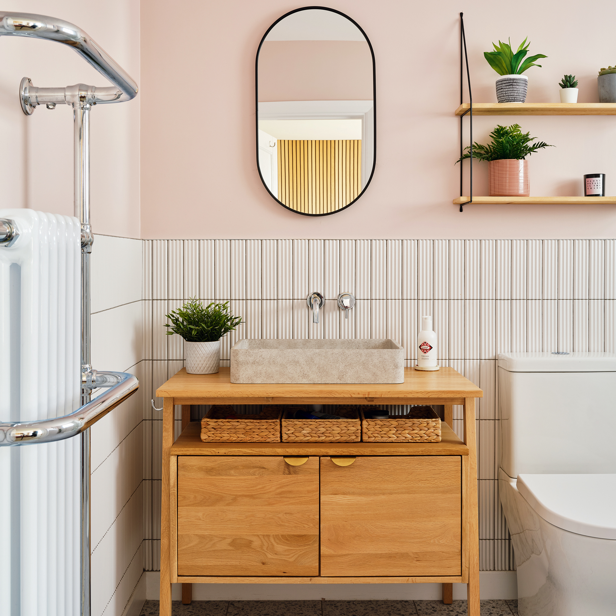 an en suite bathroom with pale pink walls and white tiling, a wooden vanity unit and an oval mirror
