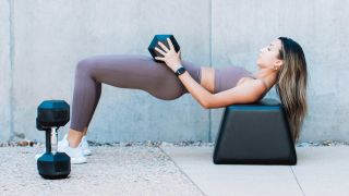 Woman performs hip thrust with dumbbell