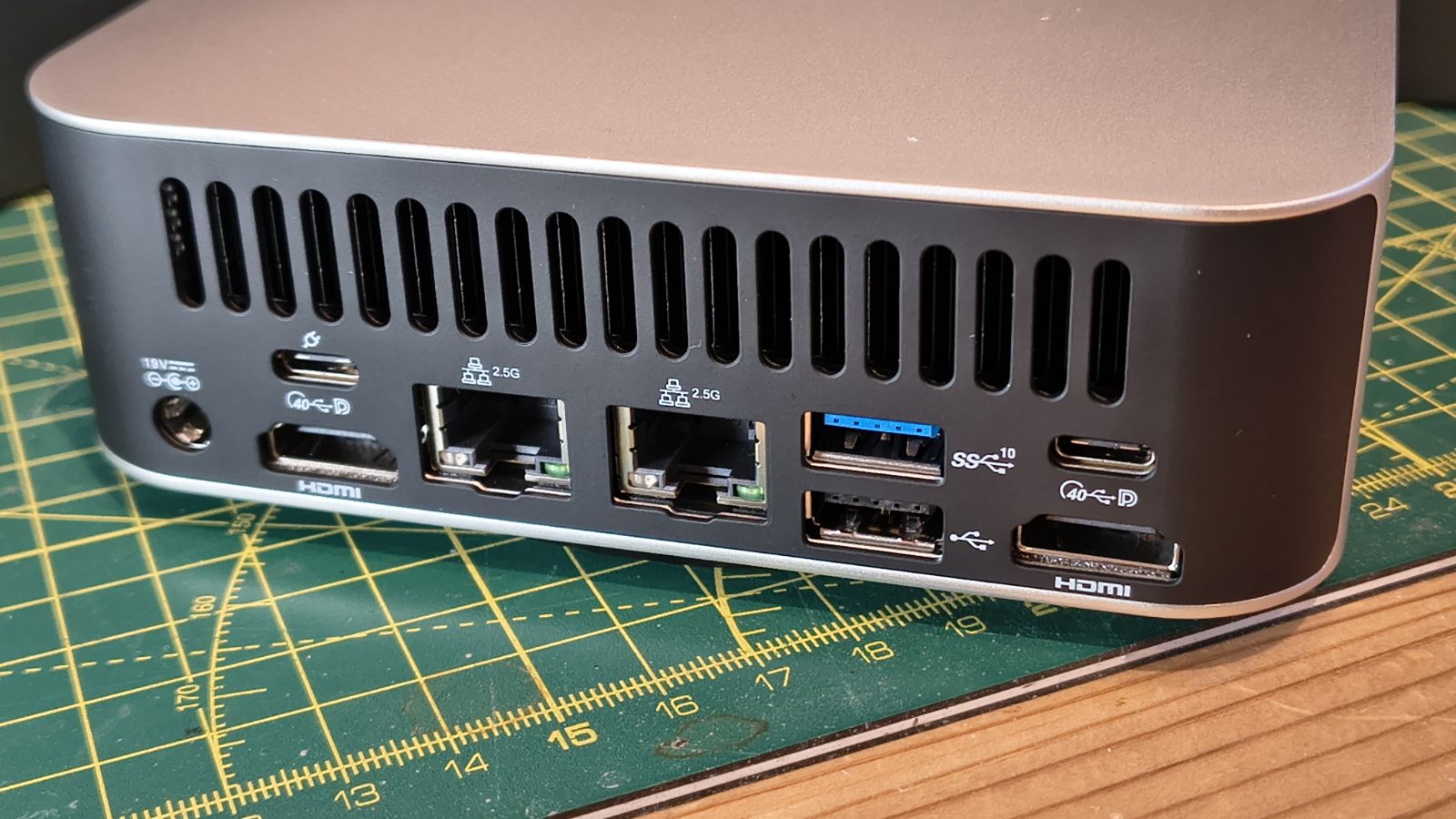 Geekom A7 Max mini PC back panel showing multiple ports including USB, HDMI, Ethernet, and USB-C, placed on a green cutting mat with measurement grid.
