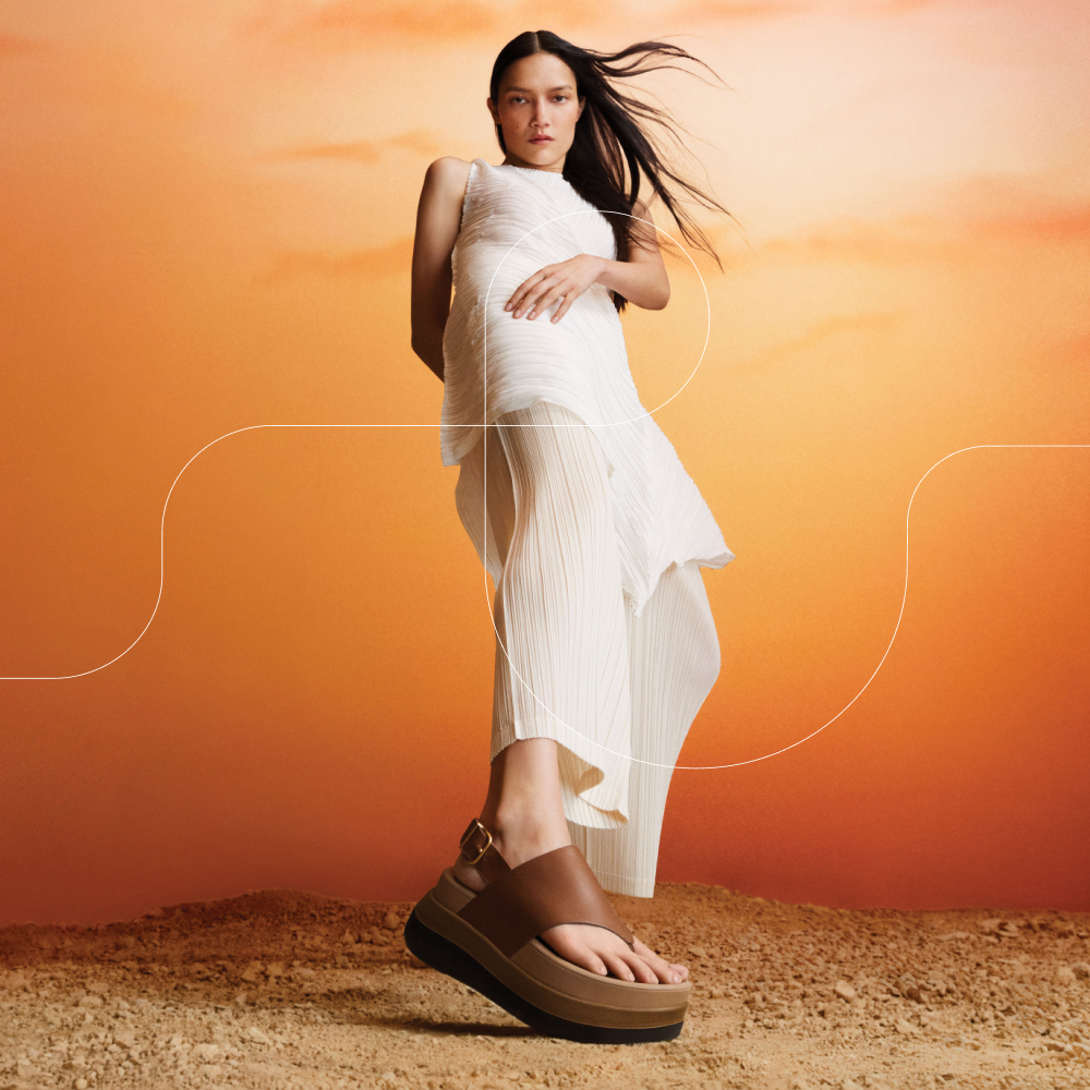 Model on a sandy floor with an orange background wearing brown FitFlop wedged sandals