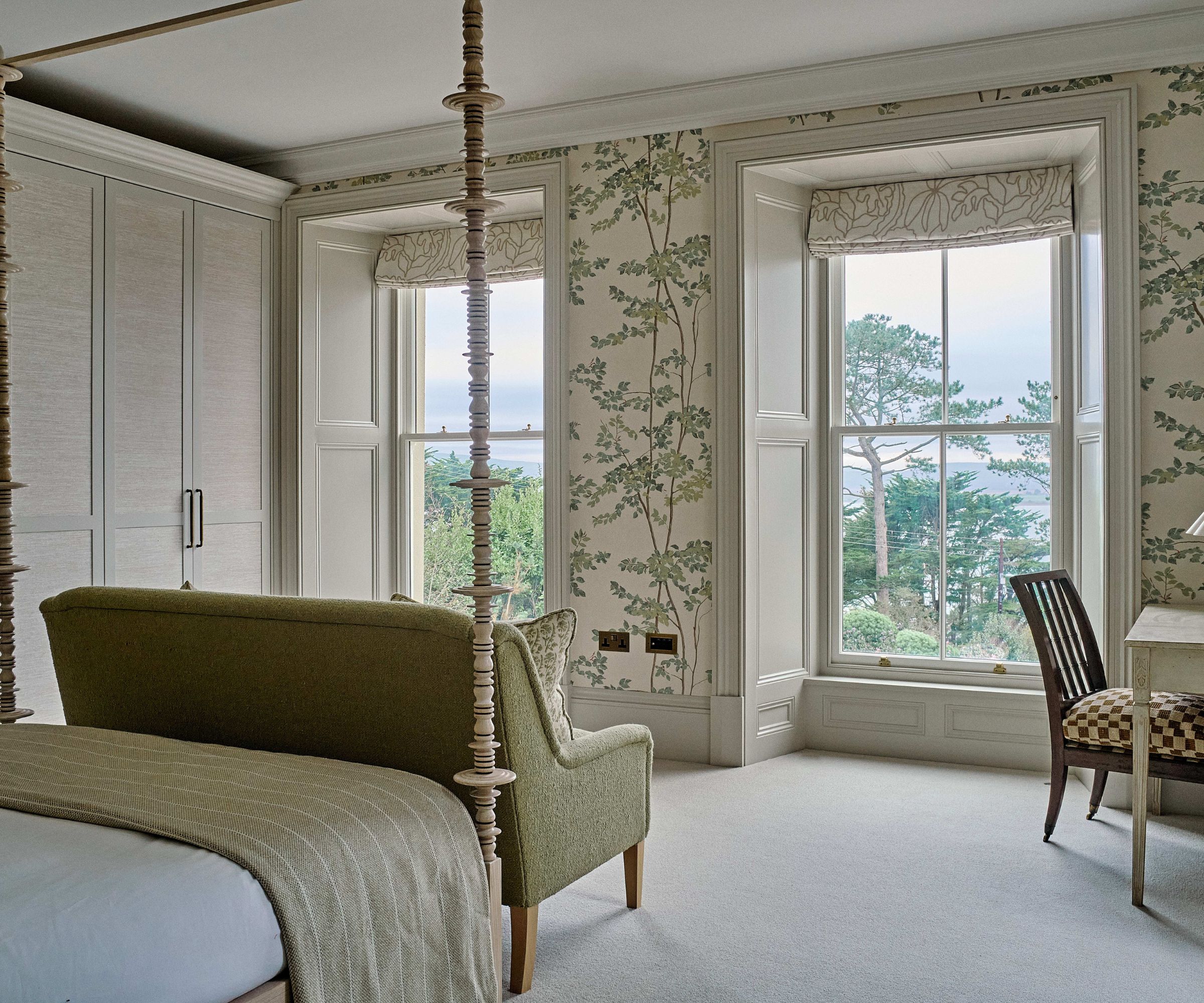Bedroom with green color scheme, four poster bed with green velvet sofa at the end and green forest print wallpaper