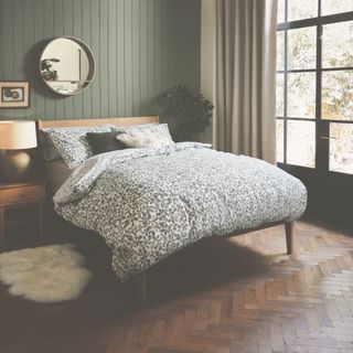 rustic bedroom with green tongue and groove wall, parquet floor, crittall doors to outside, patterned bedding, wood mirror, wood bed and matching side table, sheepkin rug