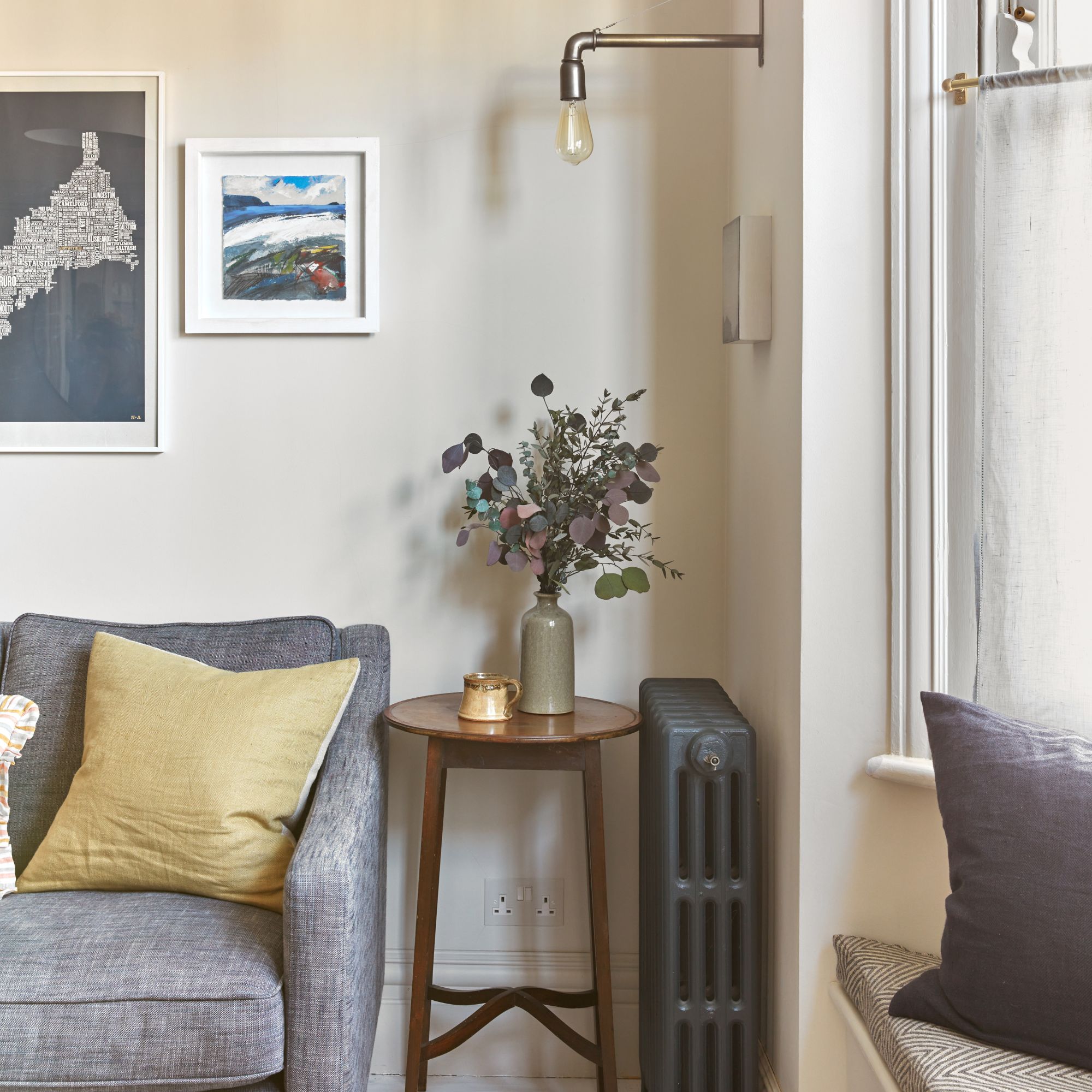 Beige painted living room with a grey sofa and a side table next to it, with a vase of flowers on it