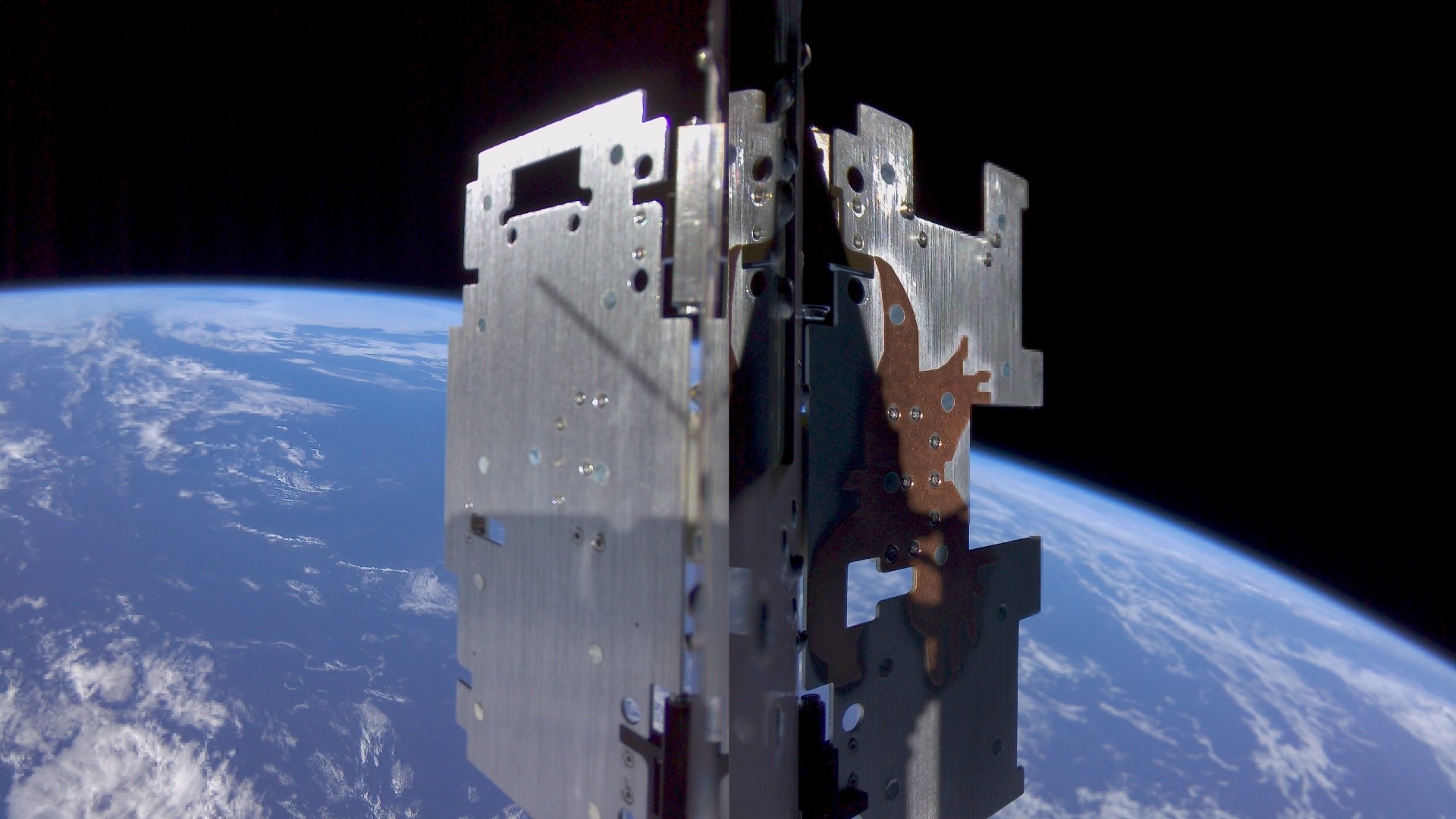 a metal cube-shaped device in the foreground with a blue-and-white earth in the background