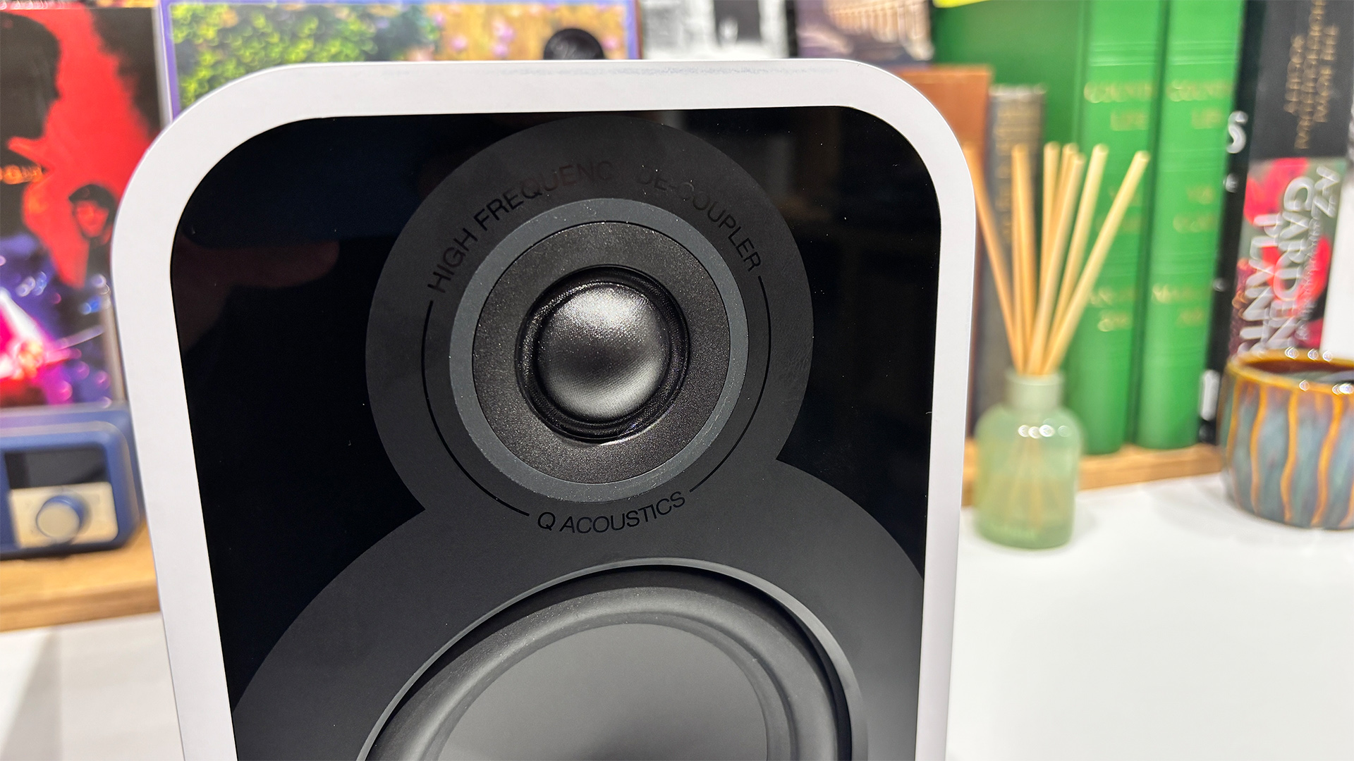 Q Acoustics 5010 standmount speakers on white surface in front of busy bookshelf, close up on tweeter